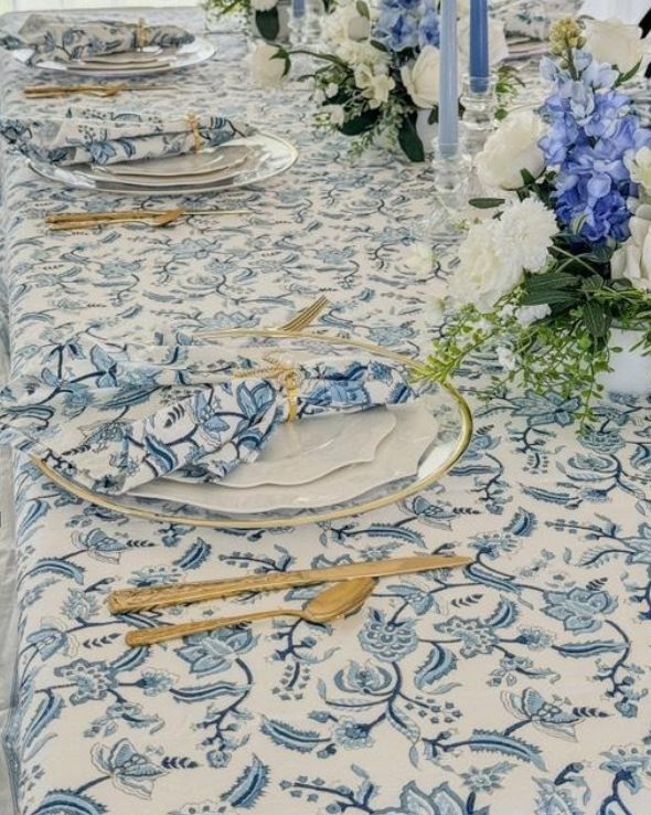 A set of four blue and white hand block printed chintz floral patterned napkins on a table with cutlery and a white tablecloth.