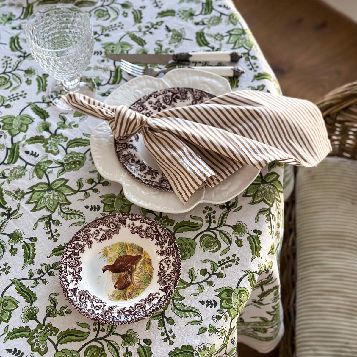 Single brown striped cotton napkin casually placed on a light brown tablecloth, creating a relaxed and inviting table setting for everyday dining.