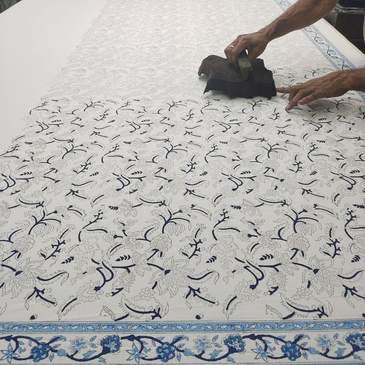 
A skilled artisan hand pressing a carved wooden block onto premium cotton fabric, printing the Chintz monochrome blue intricate floral pattern in a small batch Indian block printing process.