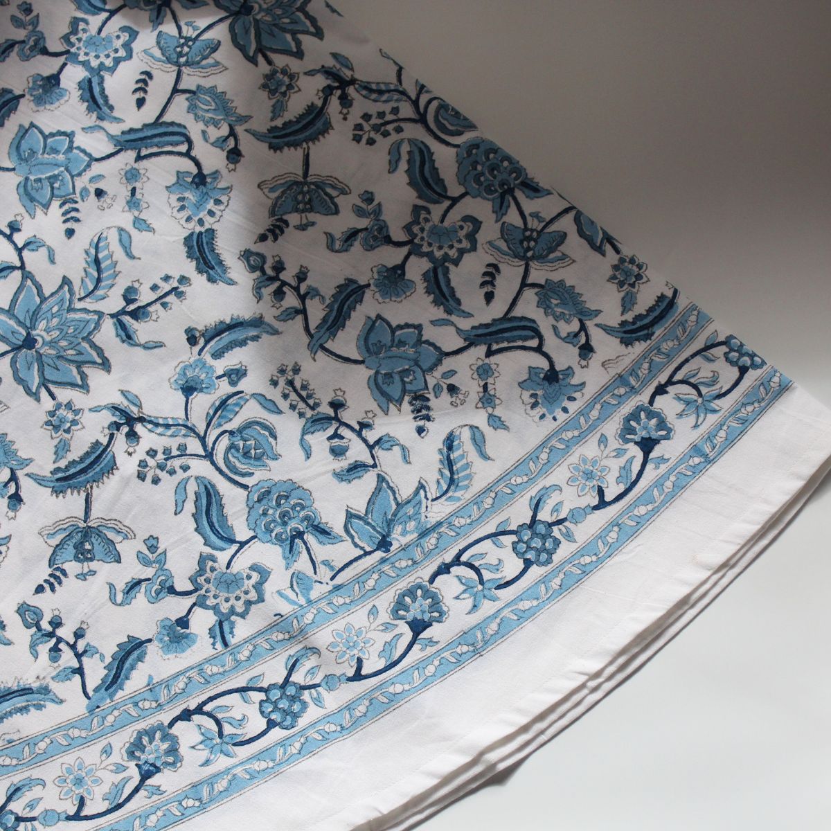 
A Chintz monochrome blue hand block printed cotton round tablecloth folded, showing the intricate floral pattern and rich decorative border on premium cotton fabric.