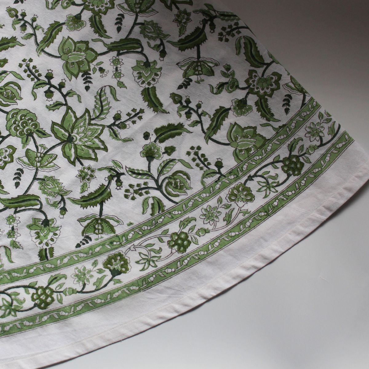 
A Chintz monochrome green hand block printed cotton round tablecloth folded flat, showing the intricate floral pattern and rich decorative border on premium cotton fabric.