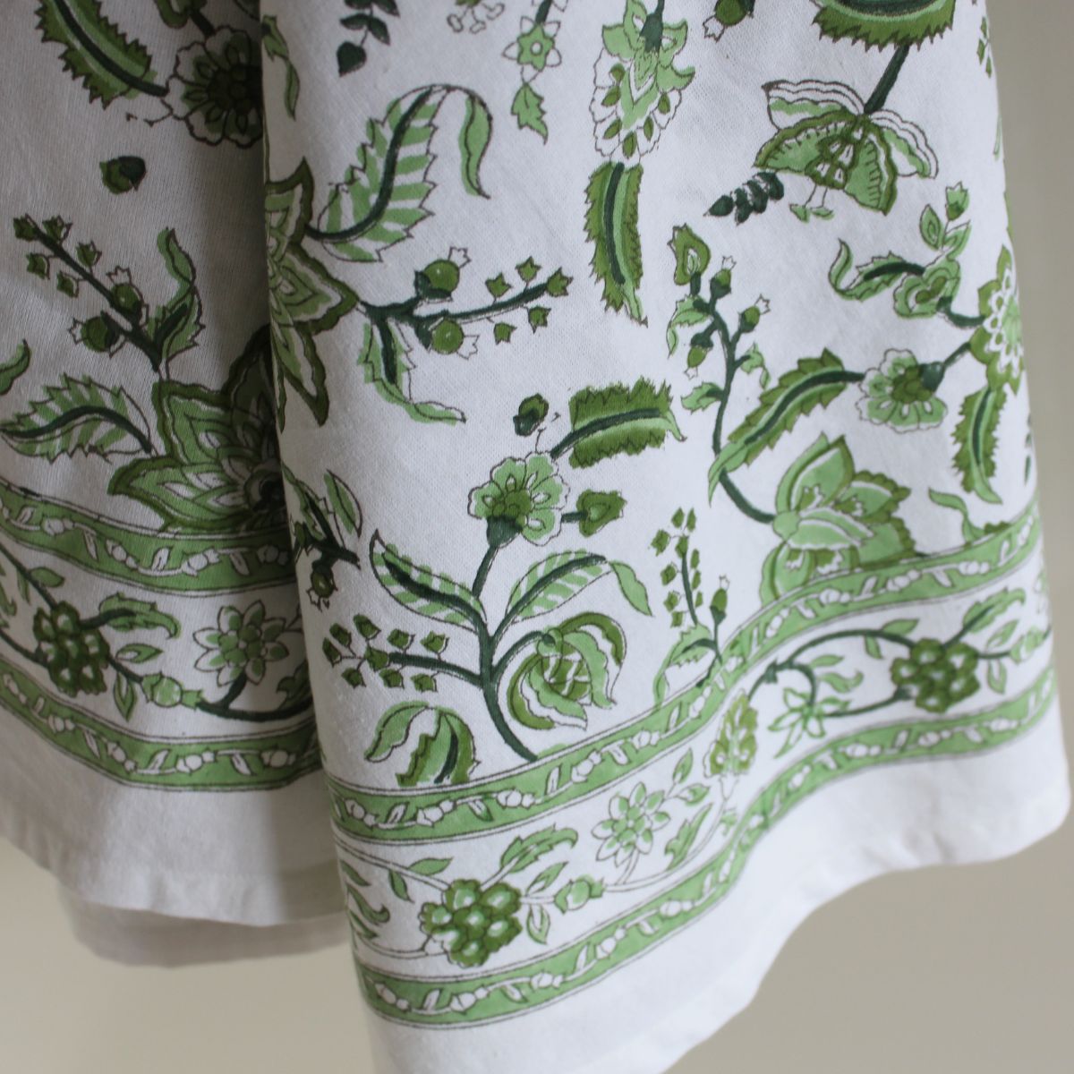 
A close-up of the Chintz monochrome green hand block printed cotton round tablecloth draped on a dining table, showing the intricate green floral motif and rich border detail on premium cotton fabric.