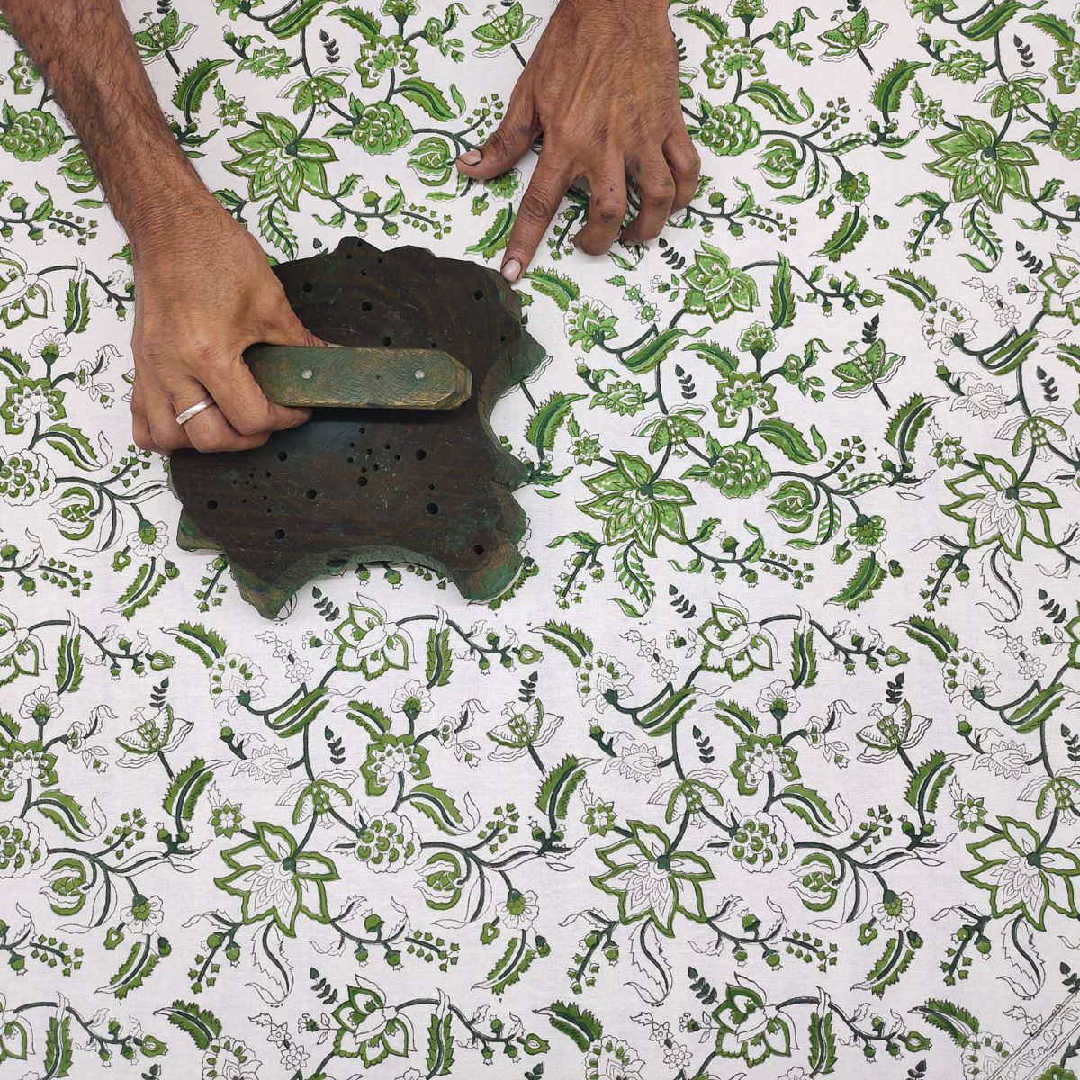 
A skilled artisan hand pressing a carved wooden block onto premium cotton, printing the Chintz monochrome green intricate floral pattern