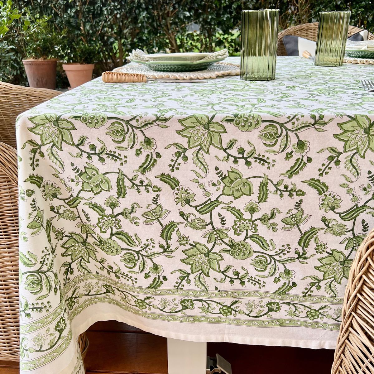Side view of 150 x 220 cm Chintz monochrome green hand block printed cotton tablecloth on a 6 seater dining table, styled for a relaxed casual meal with white and green dishes, green glasses, and striped block printed green napkins.