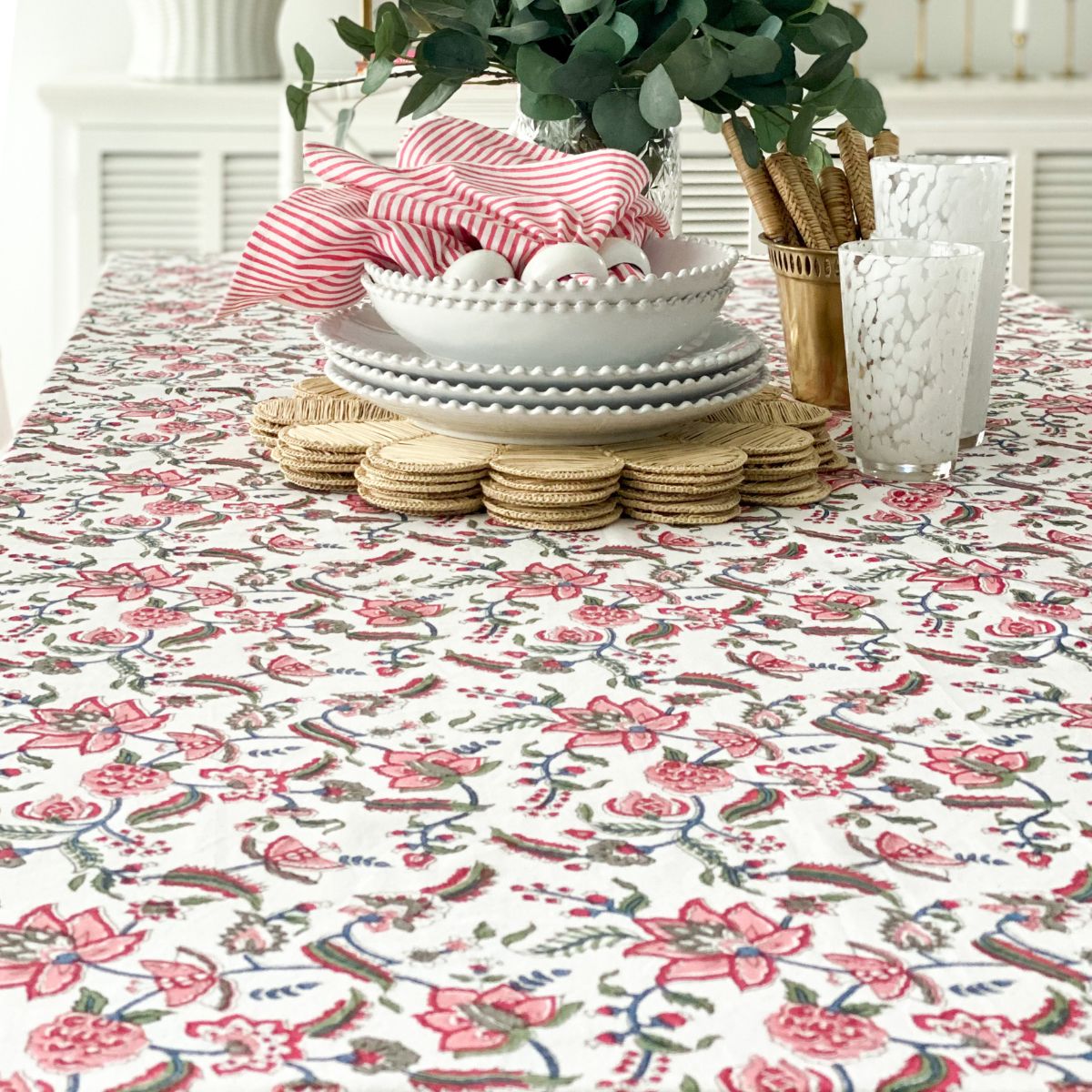 
A 220 x 220 cm Chintz multicoloured hand block printed square table linen for an 8 seater dining table, styled with a floral vase, bold and vibrant with blazing red pomegranates and green florals on premium cotton.