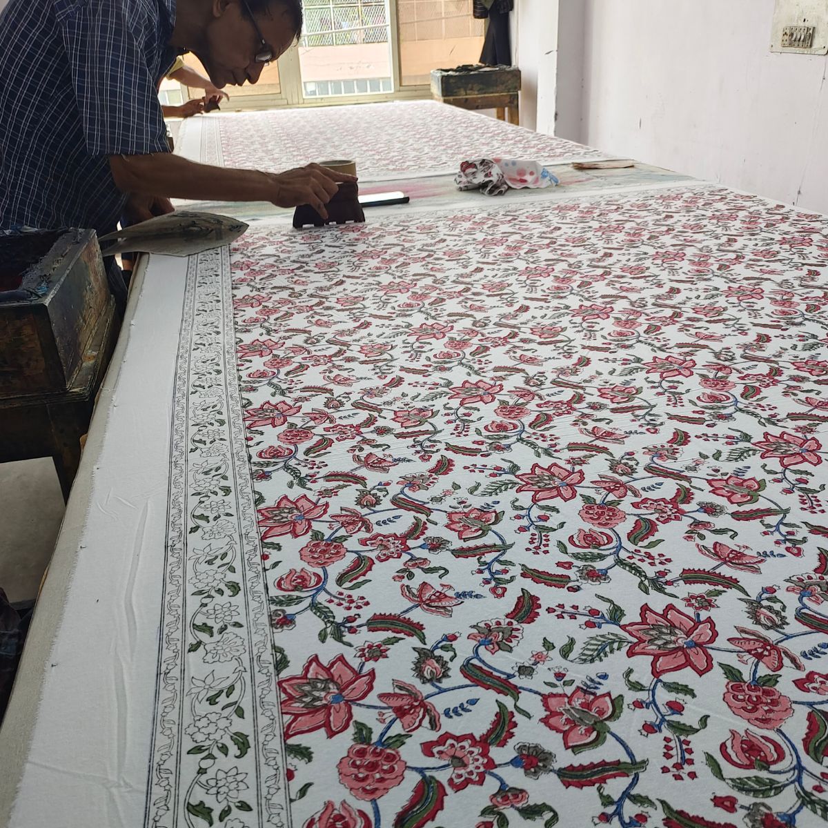 
A skilled artisan hand pressing a carved wooden block onto premium cotton, printing the Chintz multicoloured pomegranate and floral pattern, a glimpse into the small batch Indian block printing craft behind every piece.