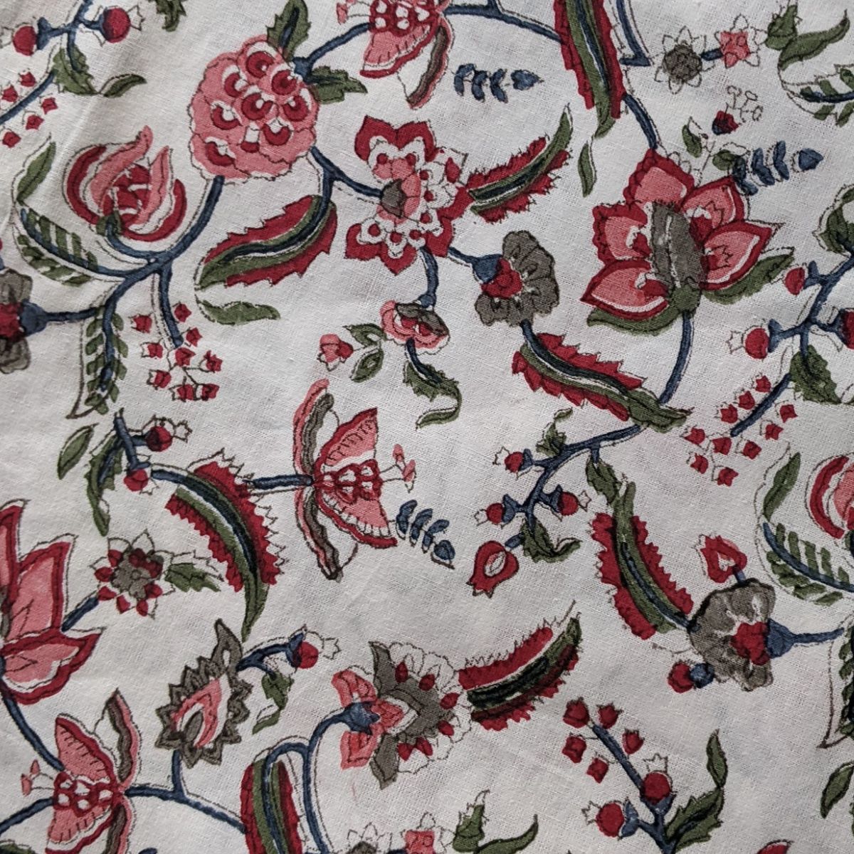 
A close-up of the Chintz multicoloured hand block printed cotton square tablecloth showing the blazing red pomegranates, lively green leaves, pretty flowers, and complementary border in rich artisan detail.