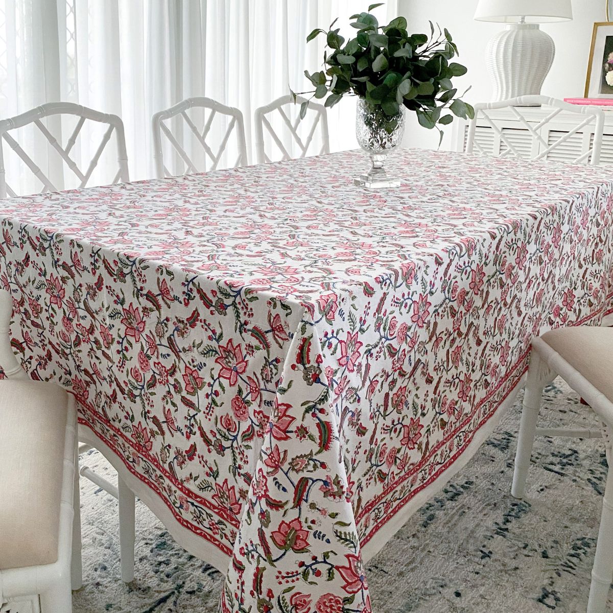 A multicolored tablecloth with a floral hand block printed pattern, featuring red hand-painted pomegranates and green leaves, displayed on a table.