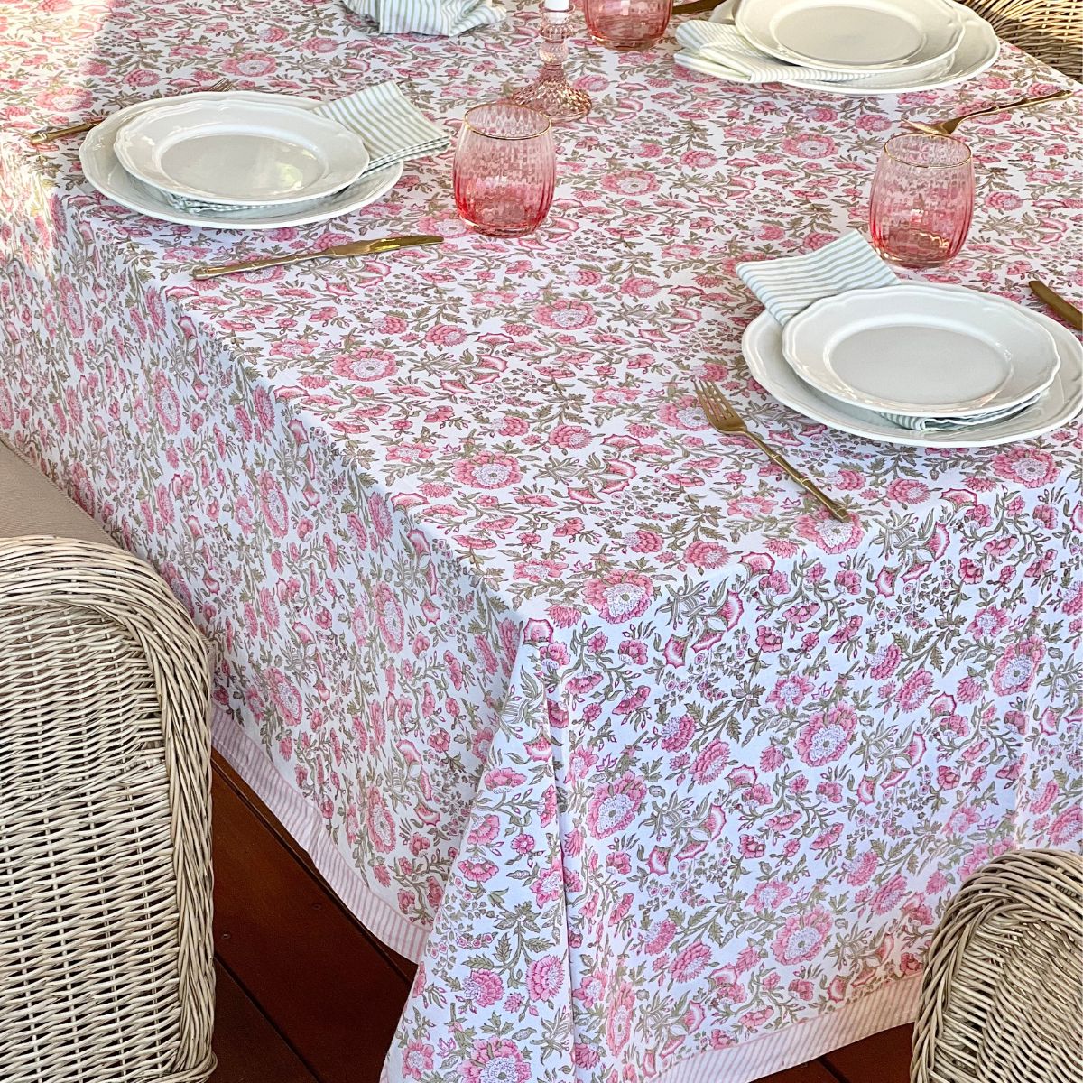 A rectangular hand block printed tablecloth in pink and green floral patterns, draped over a long dining table set with ceramic plates and linen napkins.