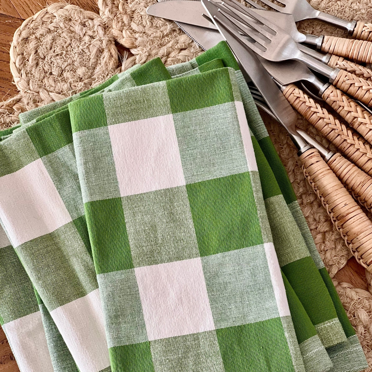 A set of 4 green gingham check handwoven cotton napkins folded neatly in a stack, showing the precision of the woven check pattern and the weight of the premium heavy duty cotton, crafted by skilled weavers in Kerala, India.
