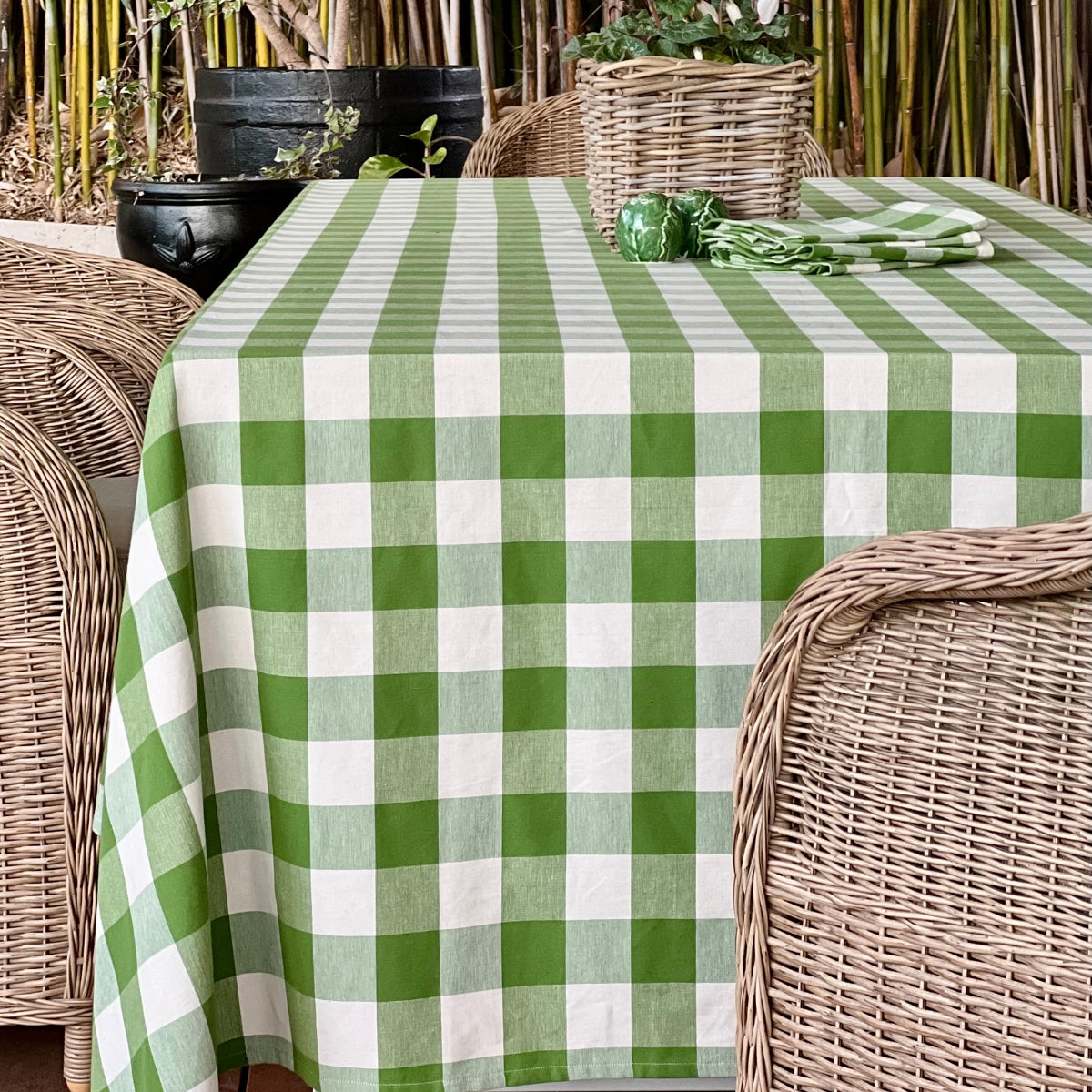 A green gingham check handwoven cotton tablecloth on a casually set dining table with decorative white plates, bamboo cutlery, green glasses, green gingham napkins in napkin rings, and a floral centrepiece, a relaxed everyday tablescape with a fresh summery feel