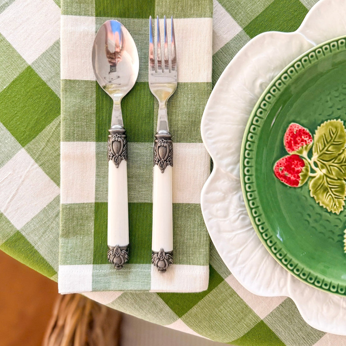 Closeup of a round green gingham check handwoven cotton tablecloth on a 4 seater table set for a relaxed lunch, with decorative plates and cutlery, matched with green checks napkins