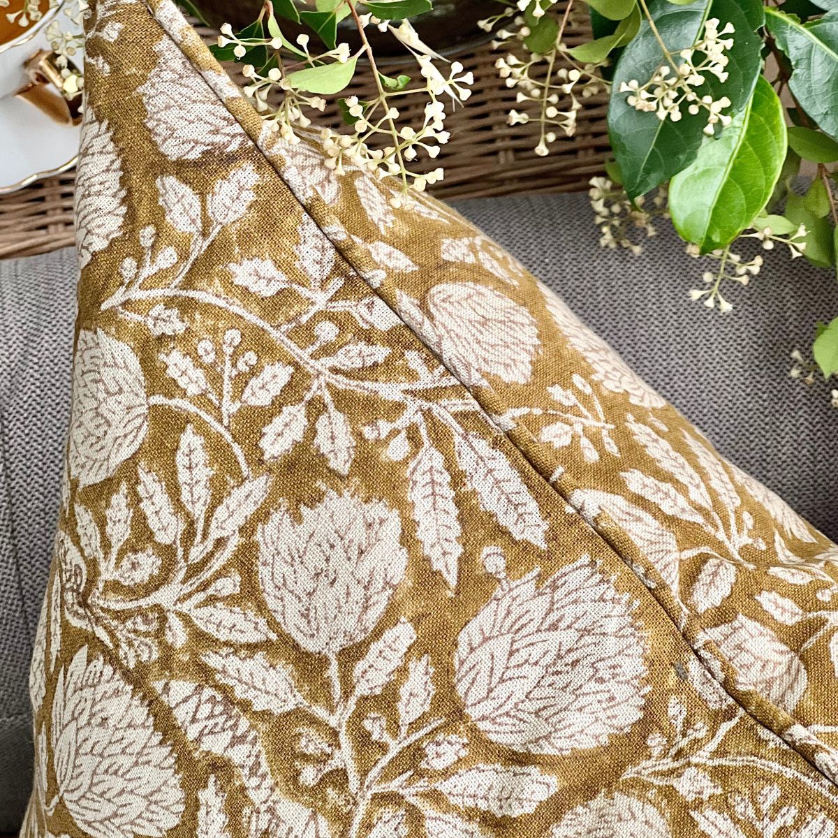 
A close-up of the Golden Flora mustard floral indian hand block printed pure linen cushion cover on a sofa, showing the bold monochrome floral motif and the natural texture of the linen fabric.