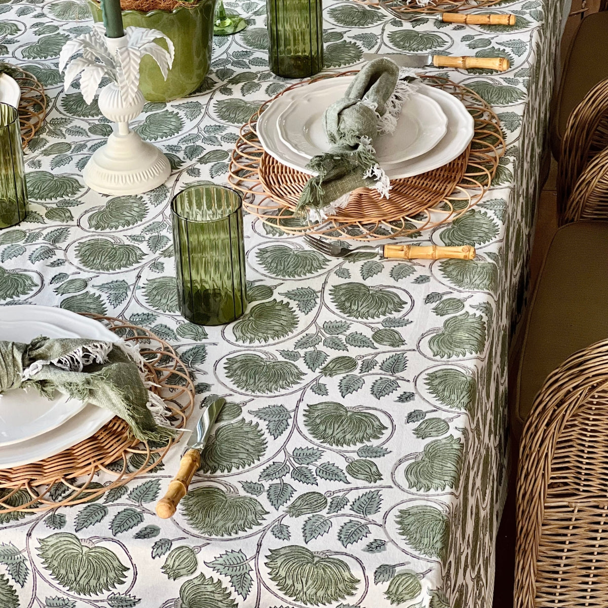 A 150 x 225 cm green lotus hand block printed cotton tablecloth on a 6 seater dining table, styled for a relaxed casual meal with green glasses, potted plants, and white dishes for a fresh botanical everyday tablescape.