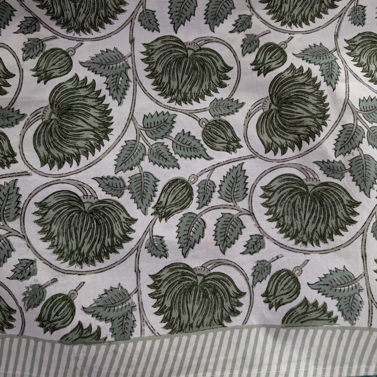 A detailed close-up of the green lotus hand block printed tablecloth fabric, the rich green floral lotus pattern with striped border, hand pressed onto premium cotton showing the texture and craft of Indian block printing.