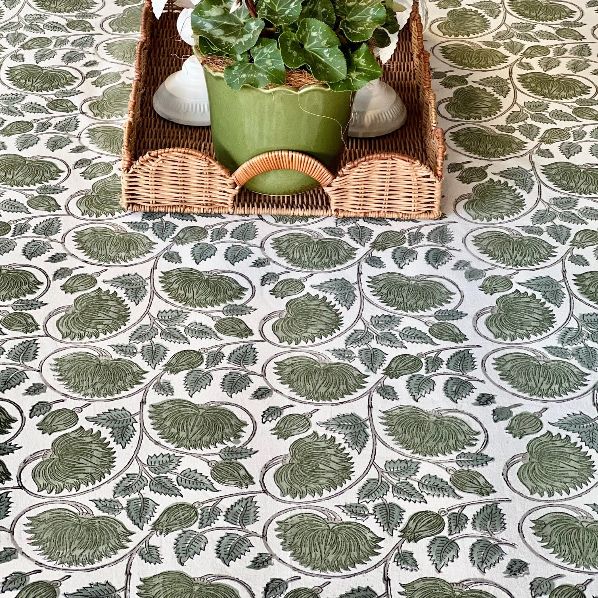 A green lotus hand block printed  tablecloth on a dining table styled with a wicker basket plant, the intricate green floral lotus print complementing the natural textures of the setting.