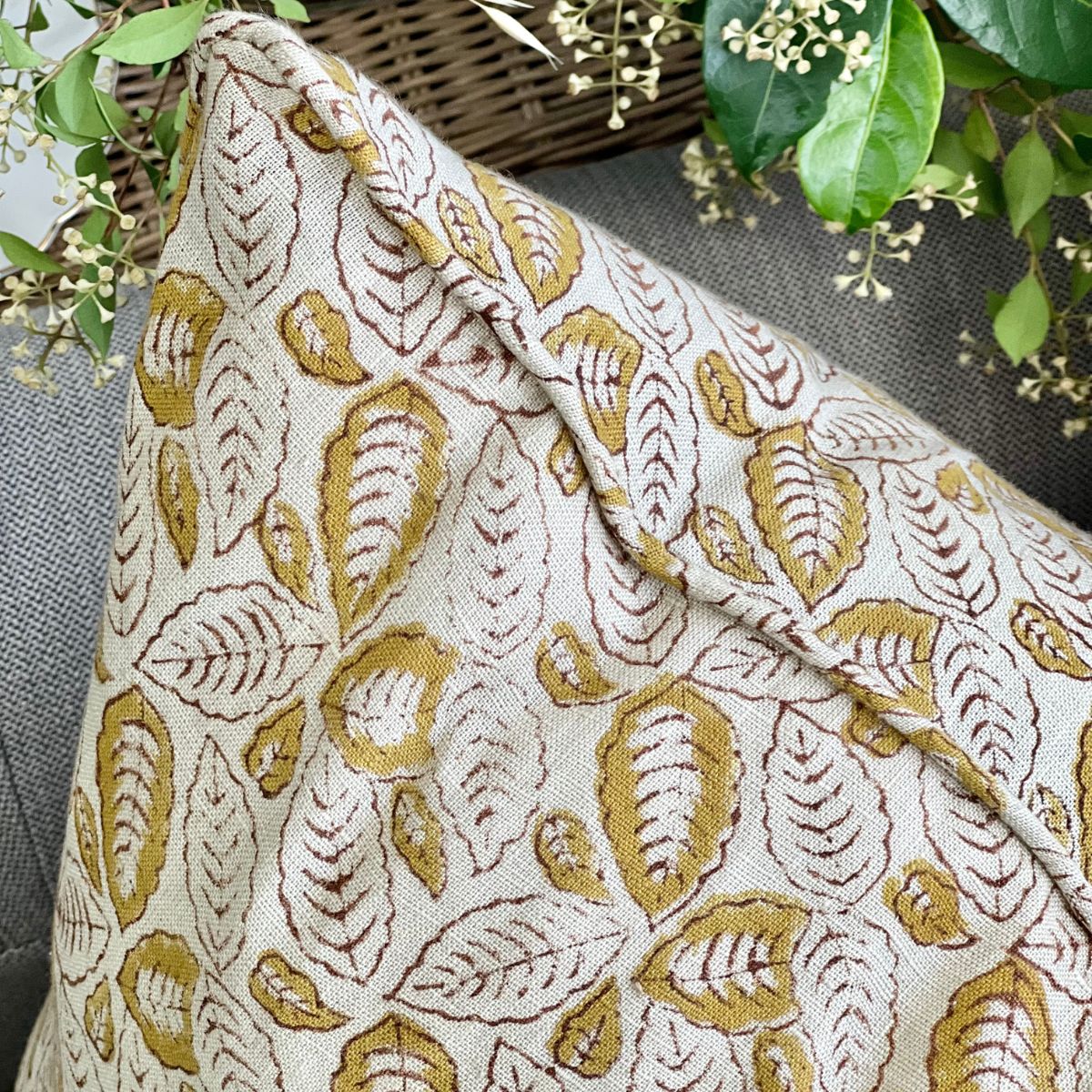 
A 50 x 50 cm Lumina Leaf hand block printed linen cushion cover, angled shot on a sofa showing the mustard leaf motif across the pure linen fabric.