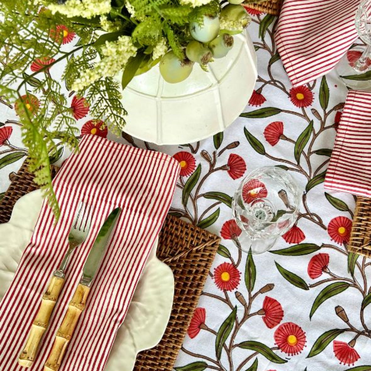 Close up view of 180 x 300 cm Red Flowering Gums tablecloth styled with dinnerware, greenery for a Christmas celebration.