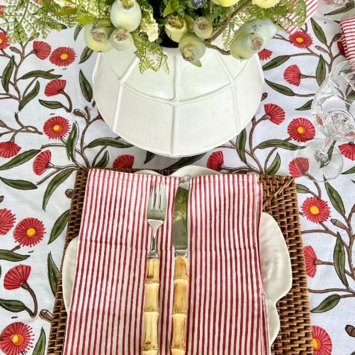 Top view of 150 x 280 cm Red Flowering Gums hand block printed tablecloth styled for an 8 to 10-seater casual lunch with white dish and red striped napkin