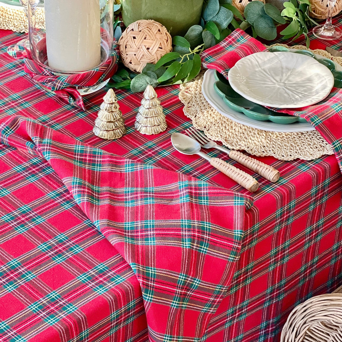 A red tartan plaid handwoven cotton tablecloth on a 6 seater Christmas table paired with red green tartan napkins, dressed with lush greenery and Christmas ornaments along the centre for a festive holiday tablescape.