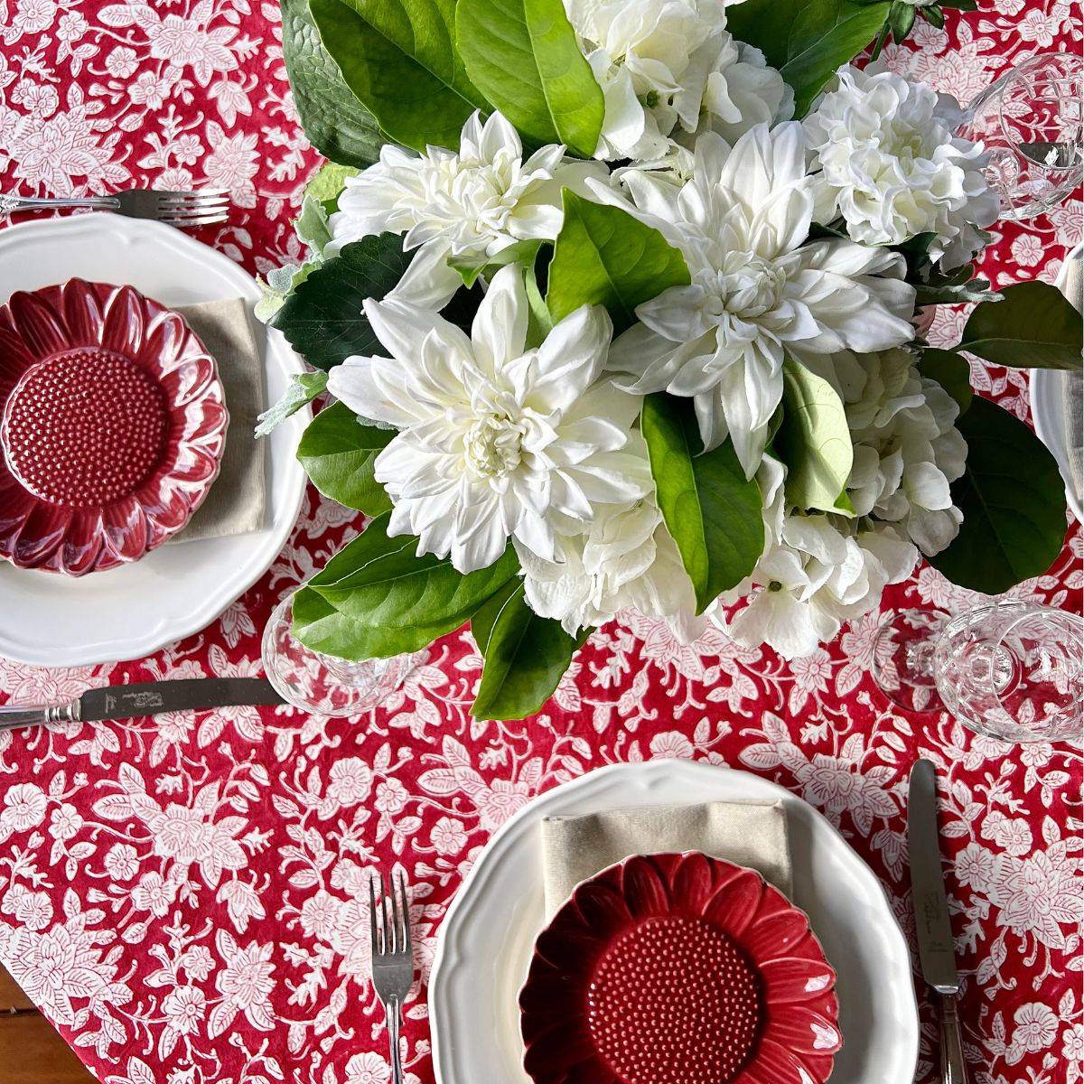 
A 150 cm red and white floral hand block printed cotton round tablecloth on a 4 seater circular dining table, styled for a relaxed casual meal with white, red floral dishes and a flower centrepiece.
