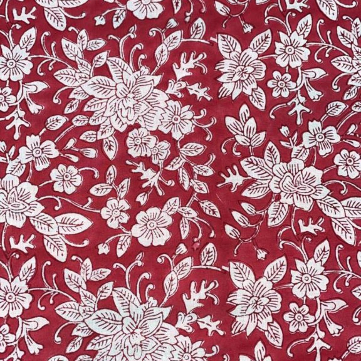 
Close up of red and white floral hand block printed cotton square tablecloth on a Christmas table, dressed with greenery along the centre, Christmas accents, and glasses for a festive holiday tablescape.