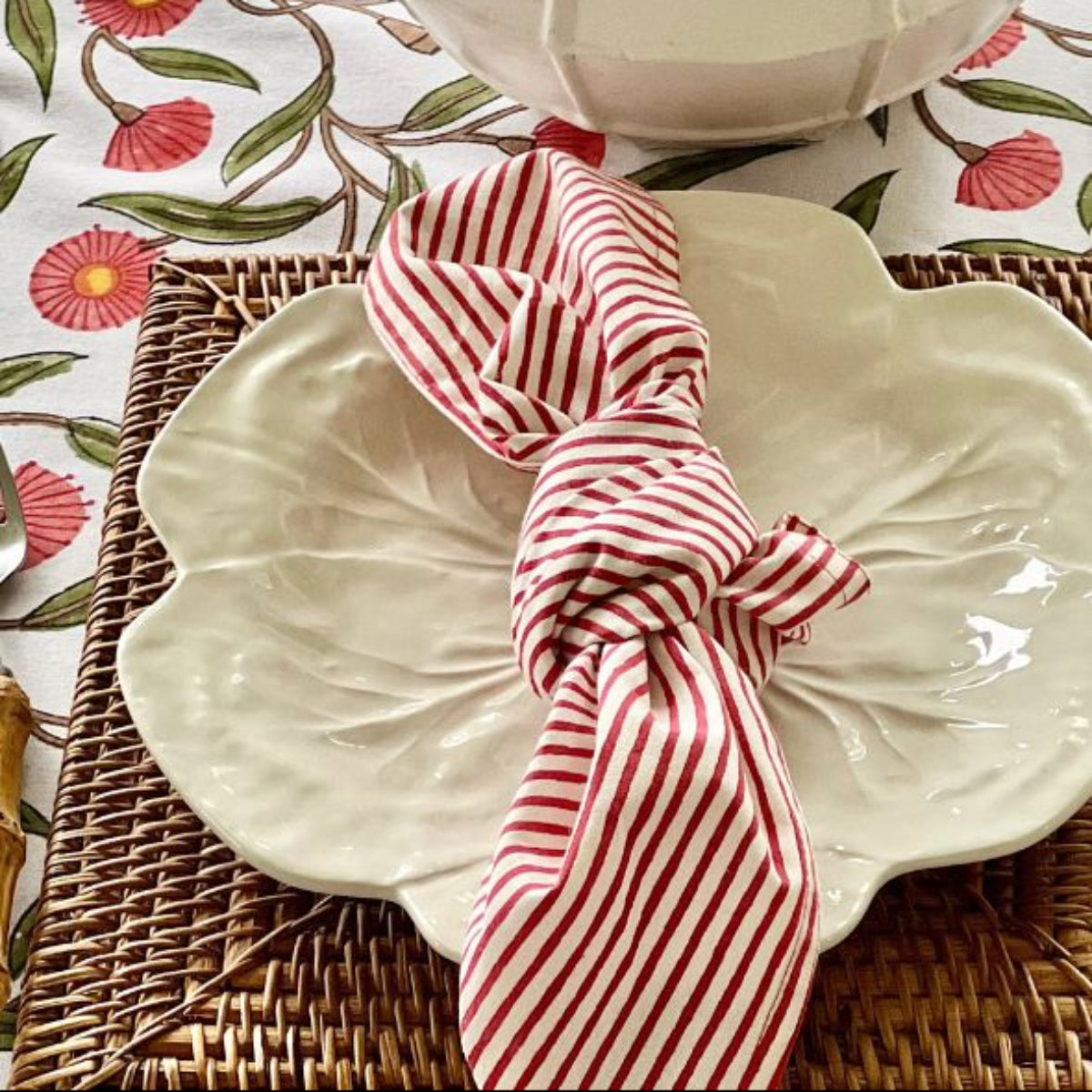 White ceramic plate with a red and white striped napkin folded in a knot style on a floral tablecloth