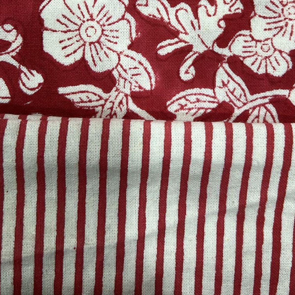 A set of red striped hand block printed table napkins with a floral pattern on the tablecloth, displayed alongside a glass of water and decorative greenery.