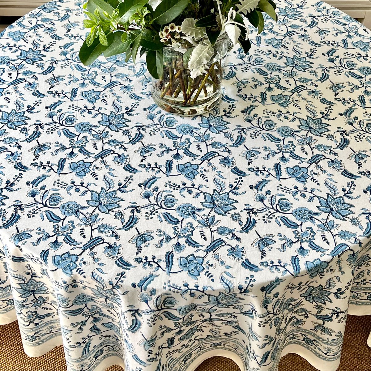A round tablecloth with a traditional blue chintz hand block printed floral pattern displayed on a table with a floral arrangement in the center.