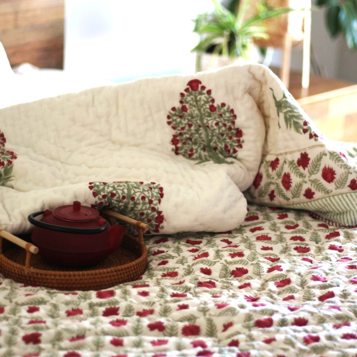
Ruby reversible cotton quilt styled with breakfast in bed and a coffee tray, featuring vibrant red and green floral block prints for a cozy morning retreat.