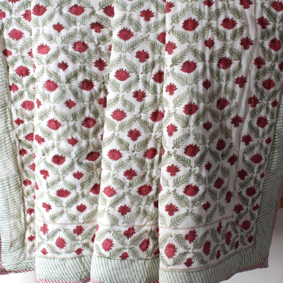 Vintage-inspired cotton quilt with elegant red and green floral block print patterns, hand quilted by artisans in Rajasthan.