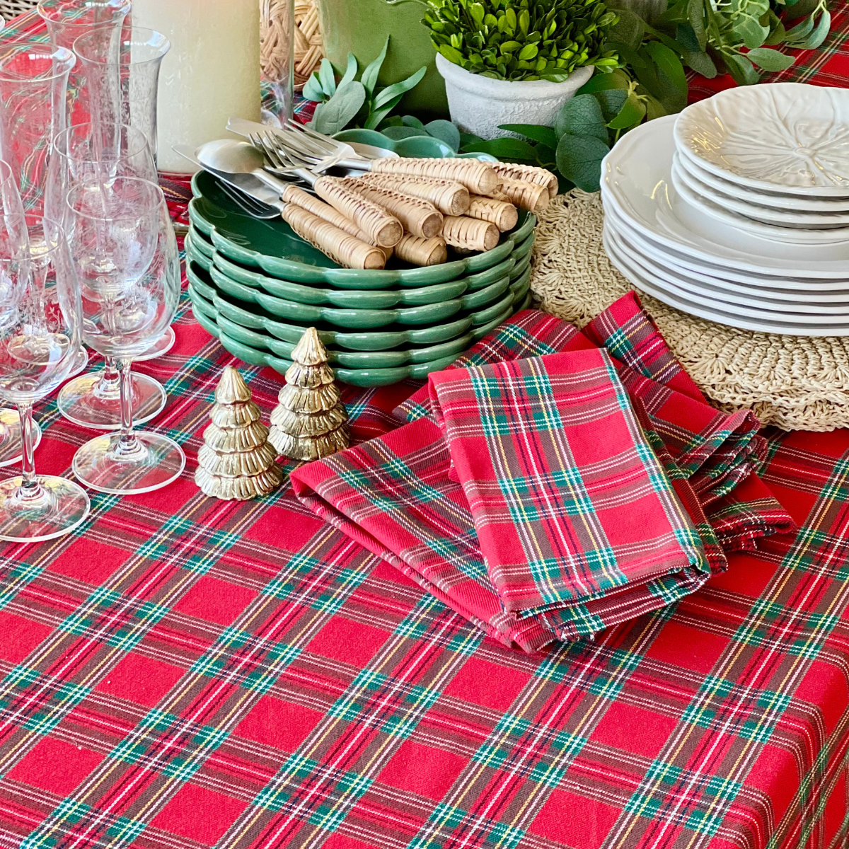 A red tartan plaid handwoven square table linen bringing warmth and bold festive cheer to a Christmas tablescape with ornaments and greenery.