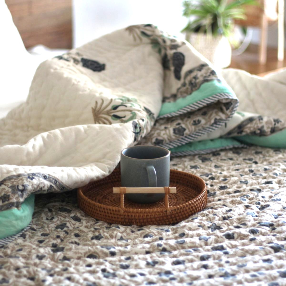 
Stella blue and green reversible cotton quilt styled for a cozy breakfast in bed with a coffee tray, showcasing hand block printed floral patterns and soft cotton comfort.