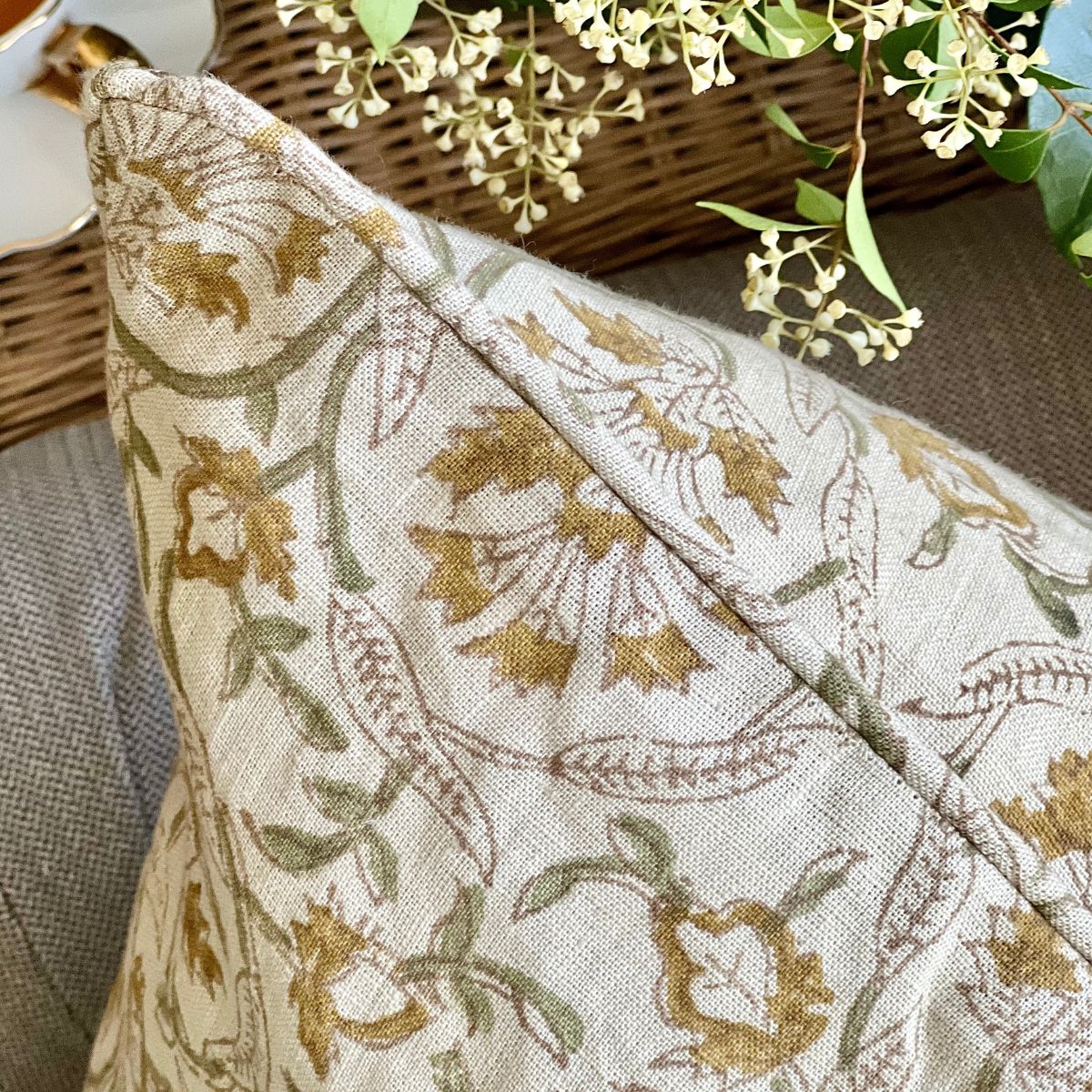 
A 50 x 50 cm Sunlit Vine hand block printed linen cushion cover, angled shot on a sofa showing the edge finish, and the delicate floral and sage green vine motif across the pure linen fabric.