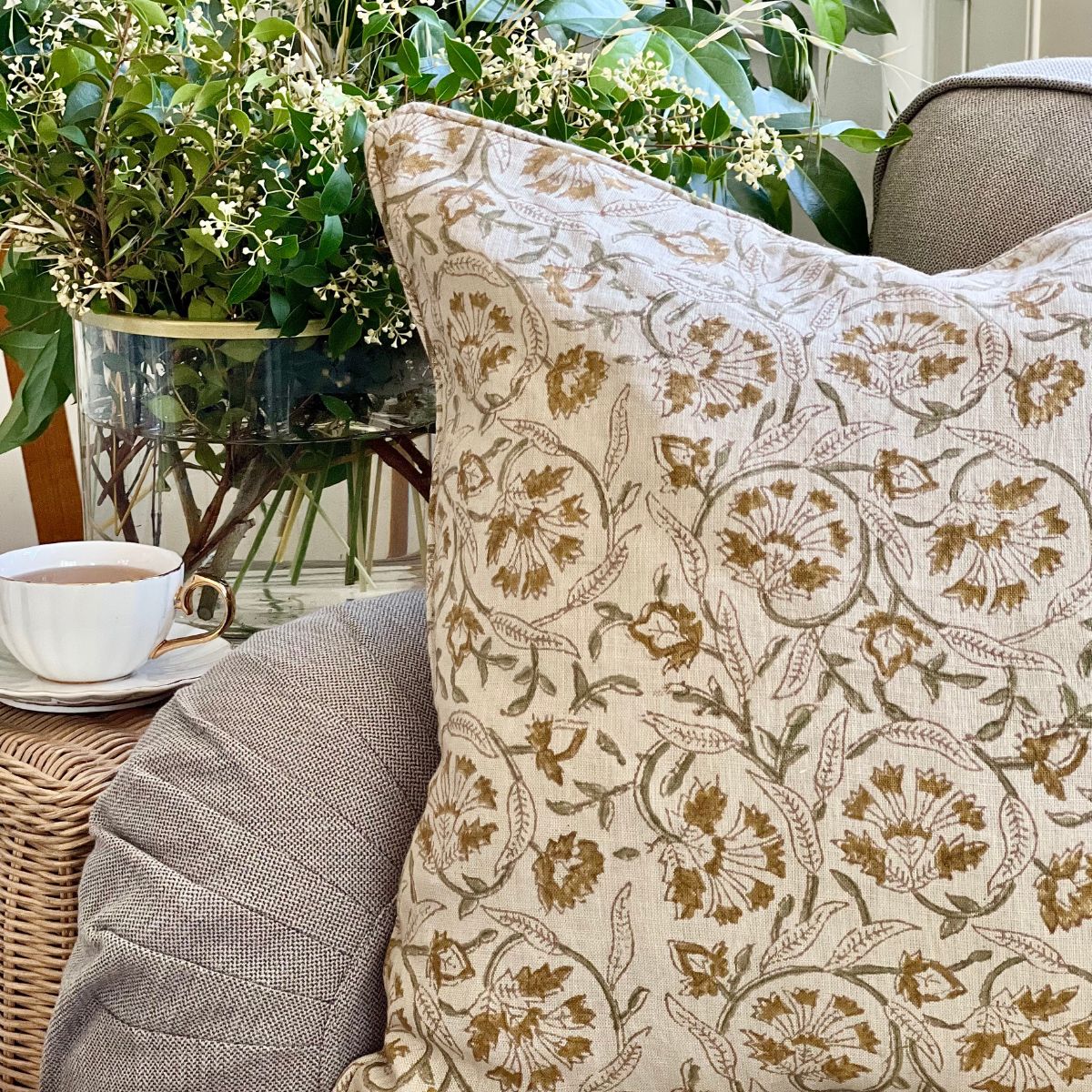 
A close-up of the Sunlit Vine hand block printed pure linen cushion cover on a sofa, showing the floral and sage green vine pattern and the natural texture of the linen fabric.