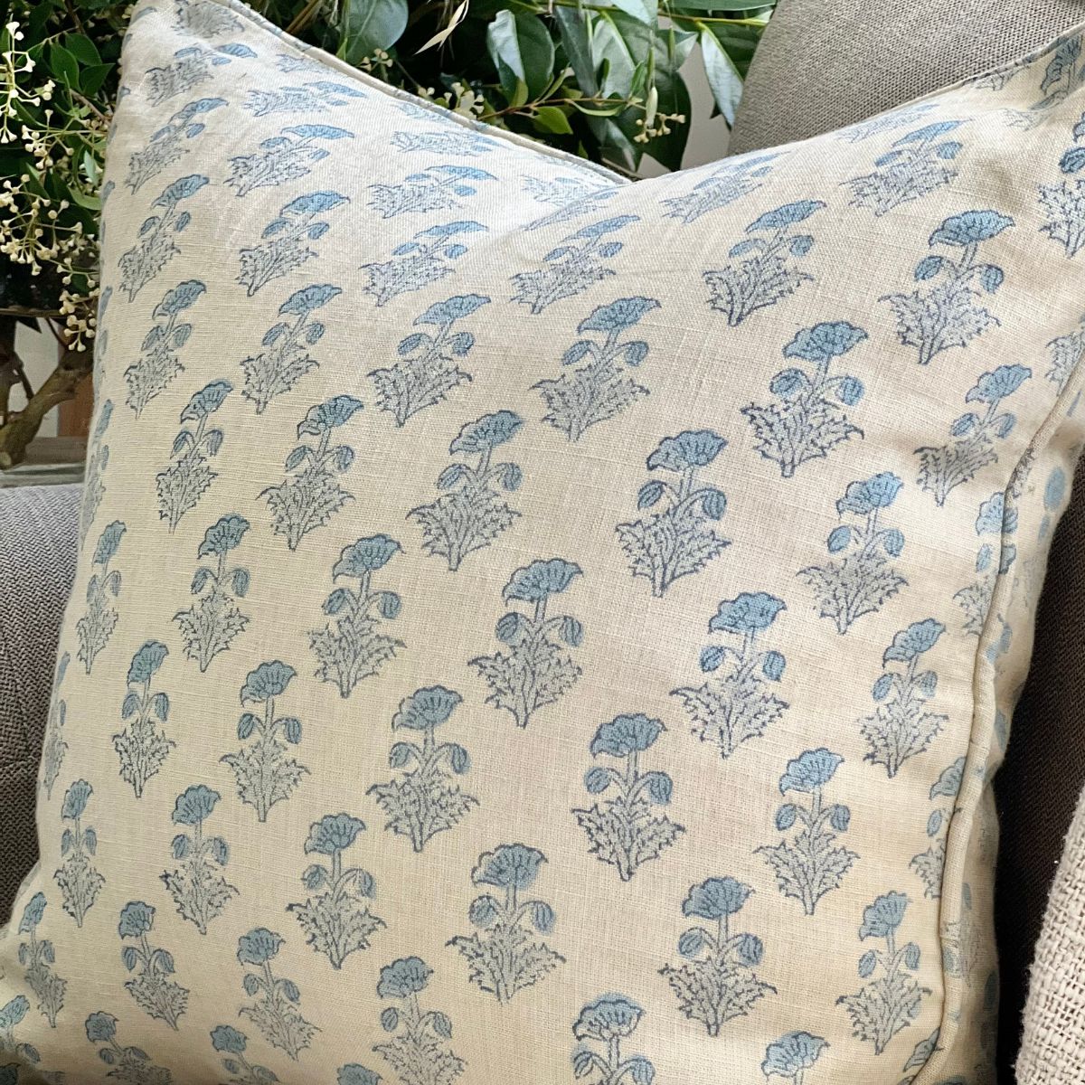 
A Tranquil Blue monochrome floral hand block printed pure linen cushion cover with zip closure and pipe edge finish, angled on a sofa in a styled living room setting.