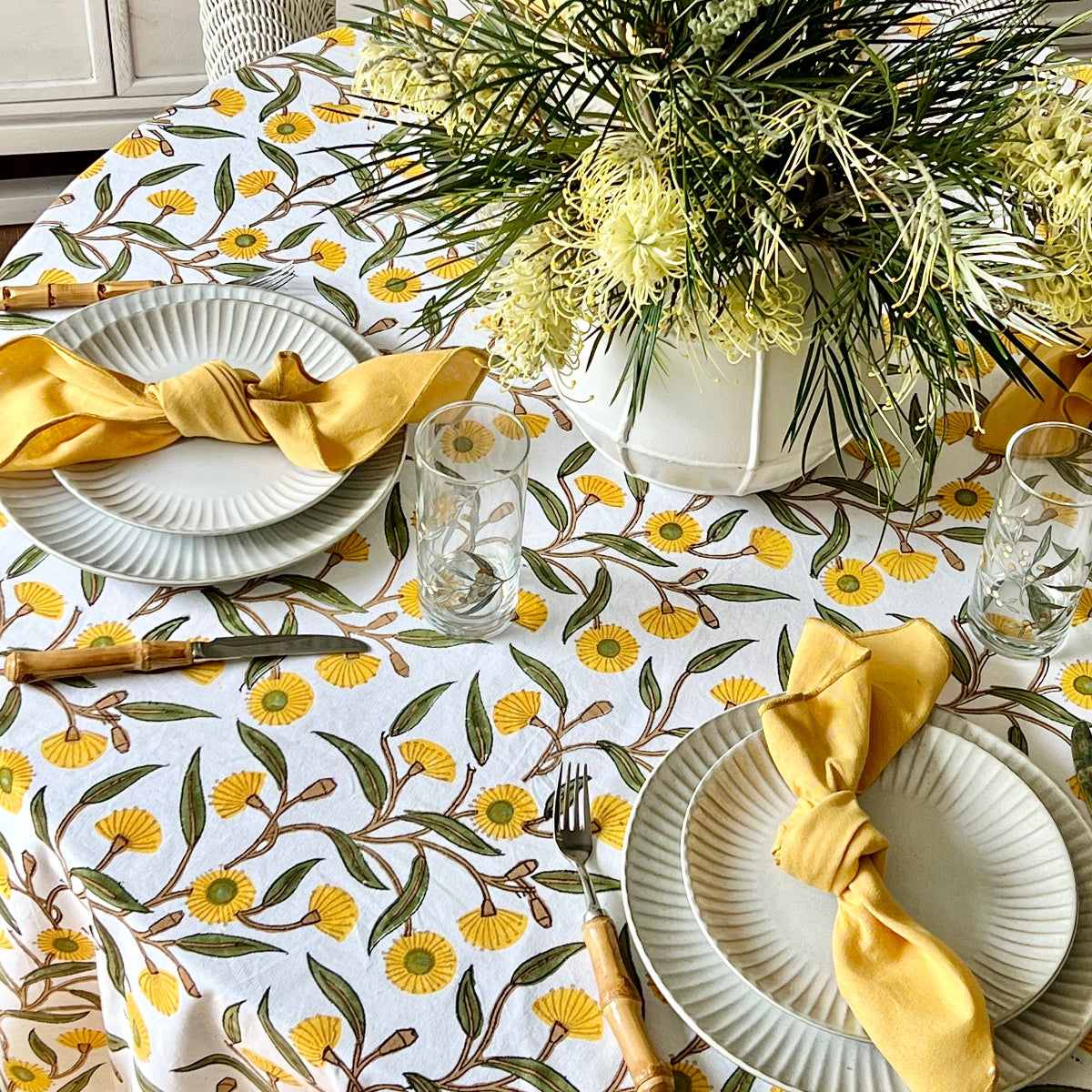 Knotted yellow napkins on dinner plates on a 180 cm Yellow Flowering Gums round tablecloth in an elegant indoor dining setting.