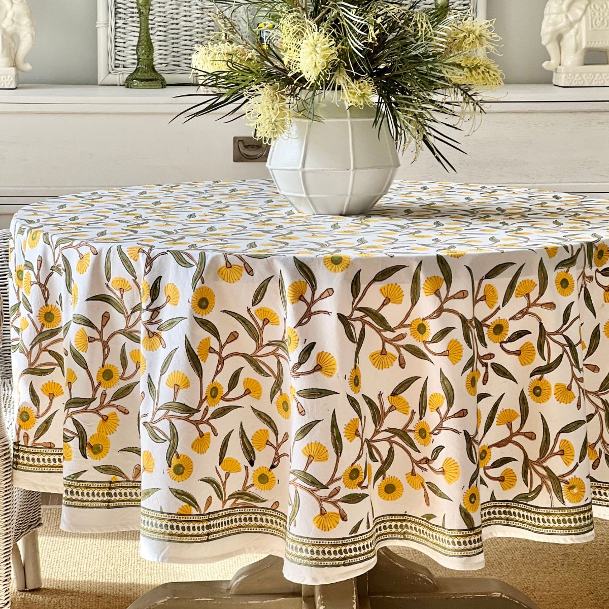 A yellow green round tablecloth with a floral hand block printed pattern featuring gum trees floral pattern, displayed on a table.
