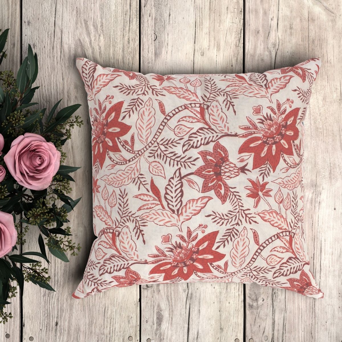 A red beige floral pattern cushion cover with a hand block printed pattern, displayed on a wooden surface next to a bouquet of pink roses.