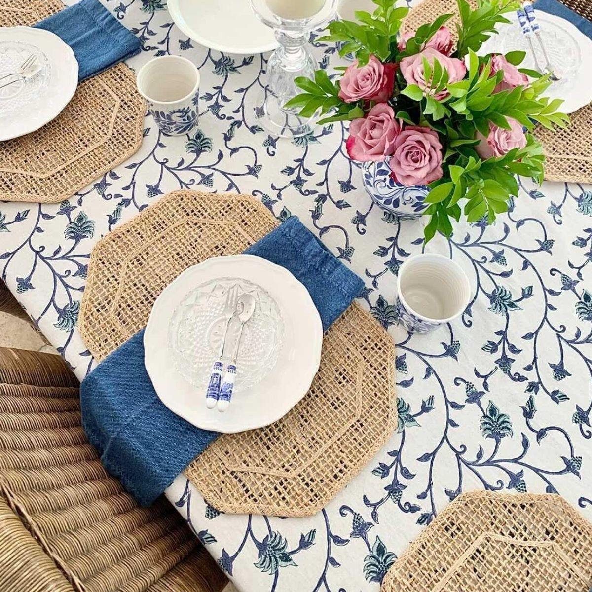  A 6 seater blue and white floral tablecloth laid on a rectangular table with rattan placemats and wicker chairs.