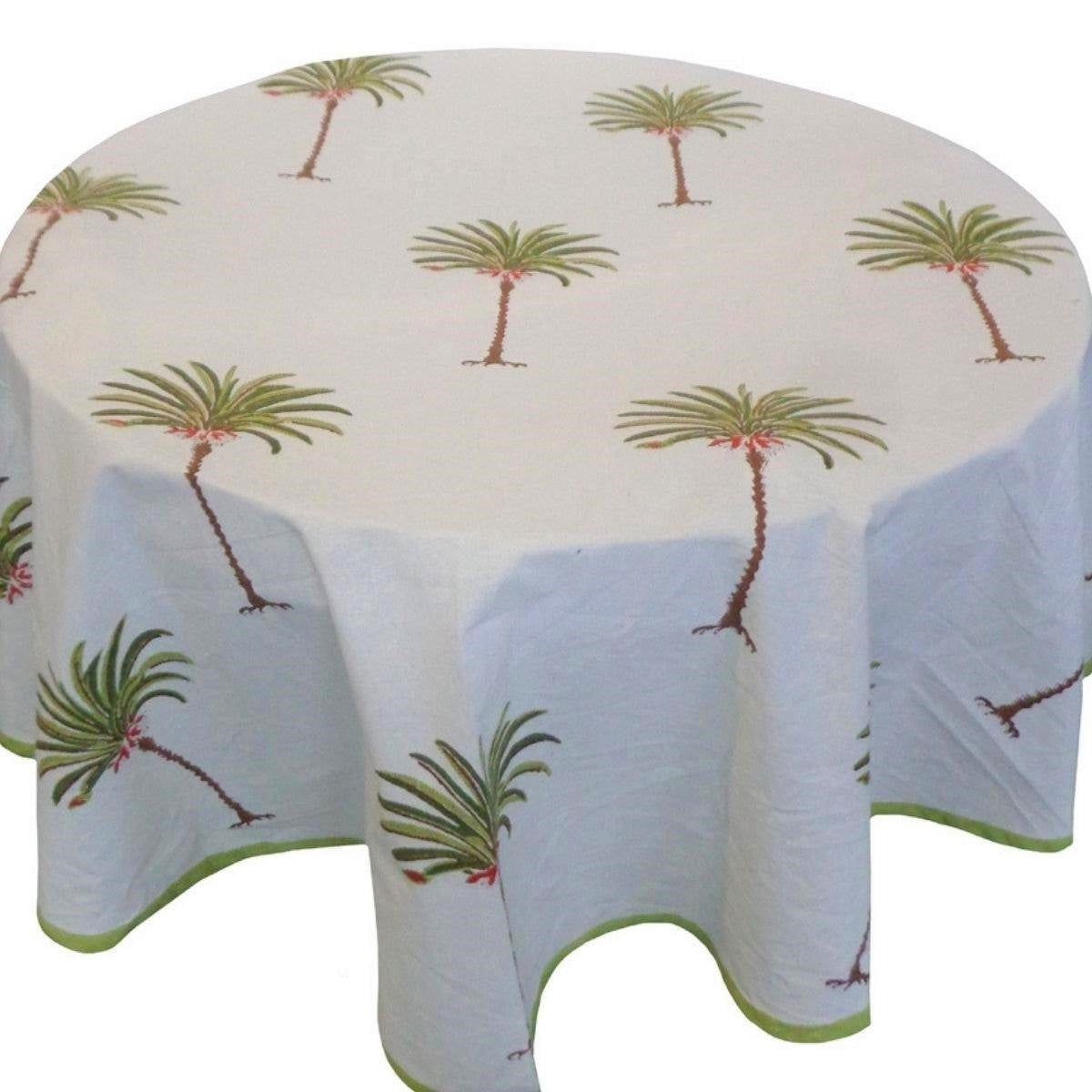 A hand block printed green round tablecloth with a pattern of tropical palm trees, displayed on a table.