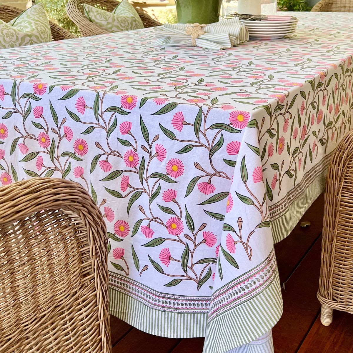 Large 180 x 340 cm Pink Green Flowering Gums tablecloth styled on a 10 to 12-seater outdoor dining table with wicker chairs, stacked dishes, and cutlery for a relaxed al fresco spring and summer gathering.