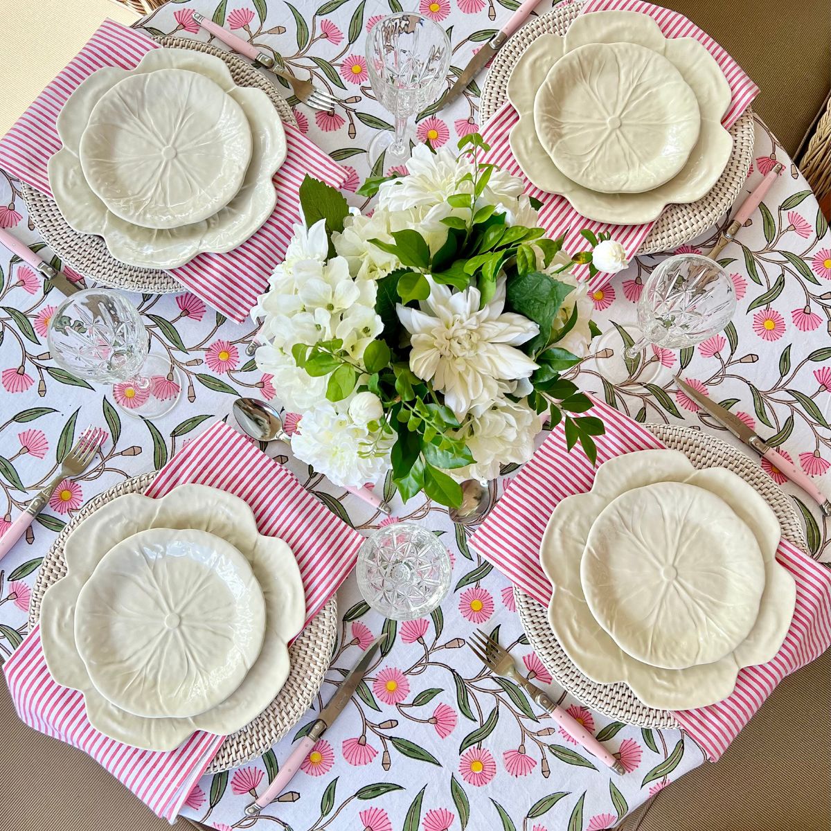 Top view of the Pink Green Flowering Gums round tablecloth styled with a matching set of four napkins, showcasing the floral pattern, geometric border, and striped edging.