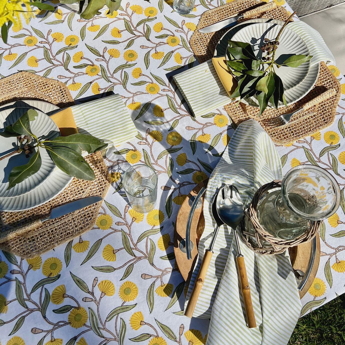 Green striped cotton napkins folded on dinnerware atop a yellow and green floral tablecloth, bringing vibrant color to brunches, garden lunches, and seasonal dining.