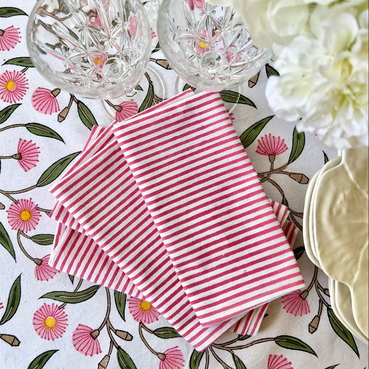 Set of 4 pink striped cotton napkins hand block printed by artisans, folded on a pink and green floral tablecloth for everyday dining and casual gatherings.