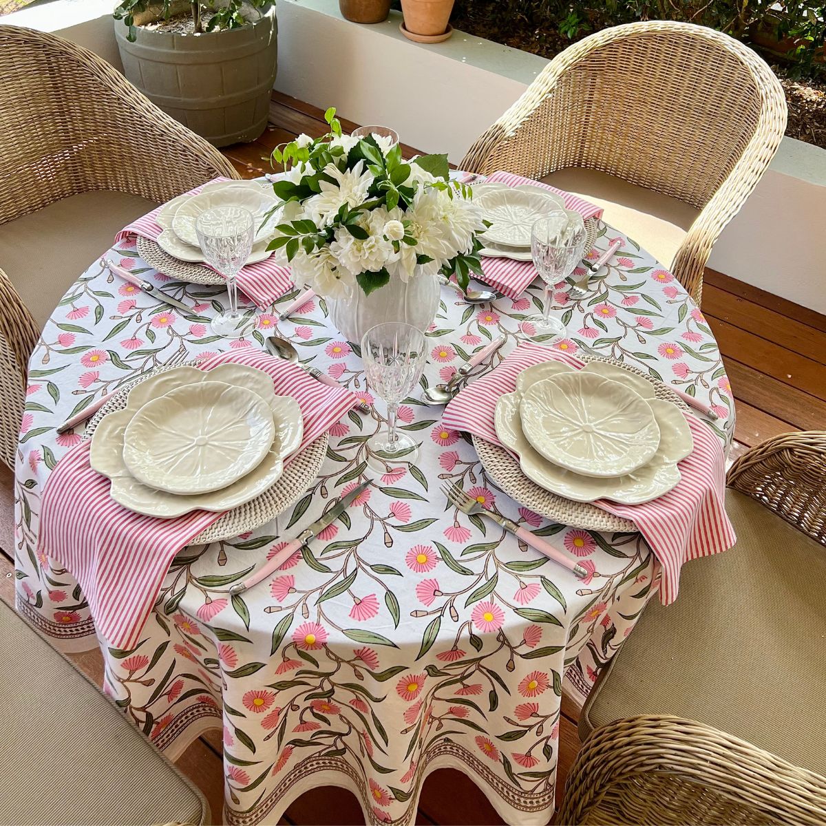 Round table setting featuring folded pink striped cotton napkins beneath white dinner plates, styled for family meals, brunches, and special occasions.