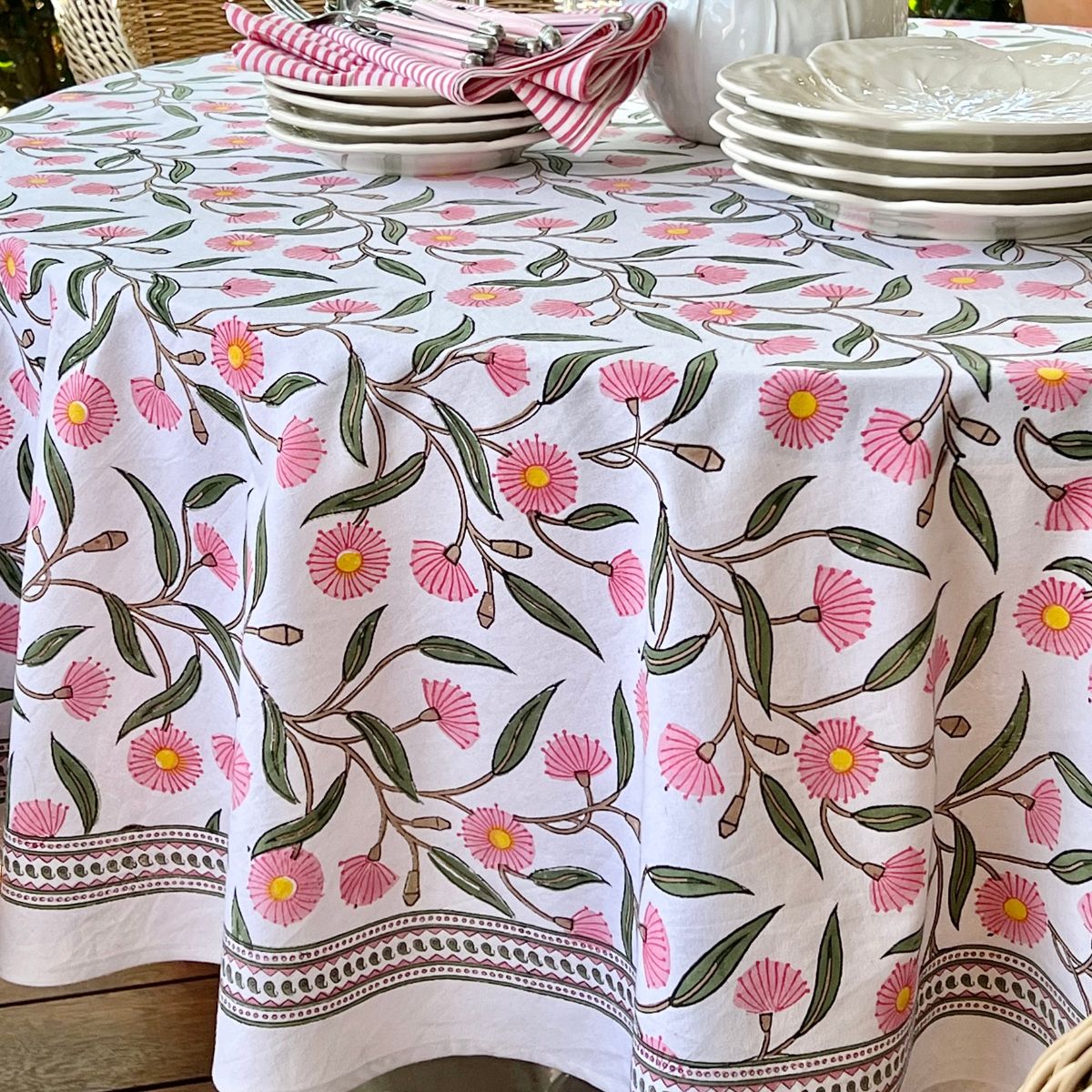 A hand block printed round tablecloth with a flowering gums  floral pattern in pink and green, displayed on a table.