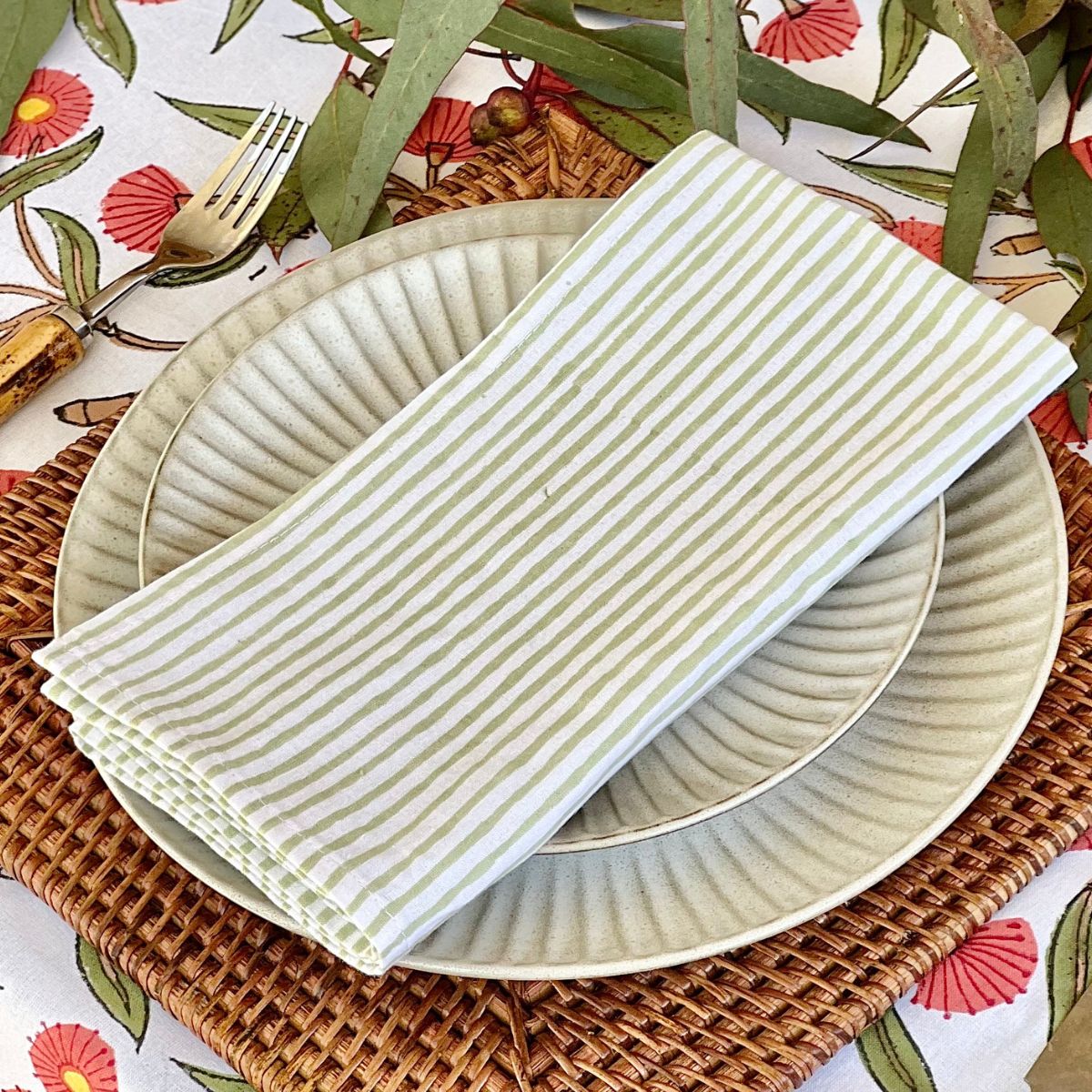 Close up view of 180 cm Red Flowering Gums round tablecloth set for a casual family lunch with coordinating tableware and striped green cotton napkins
