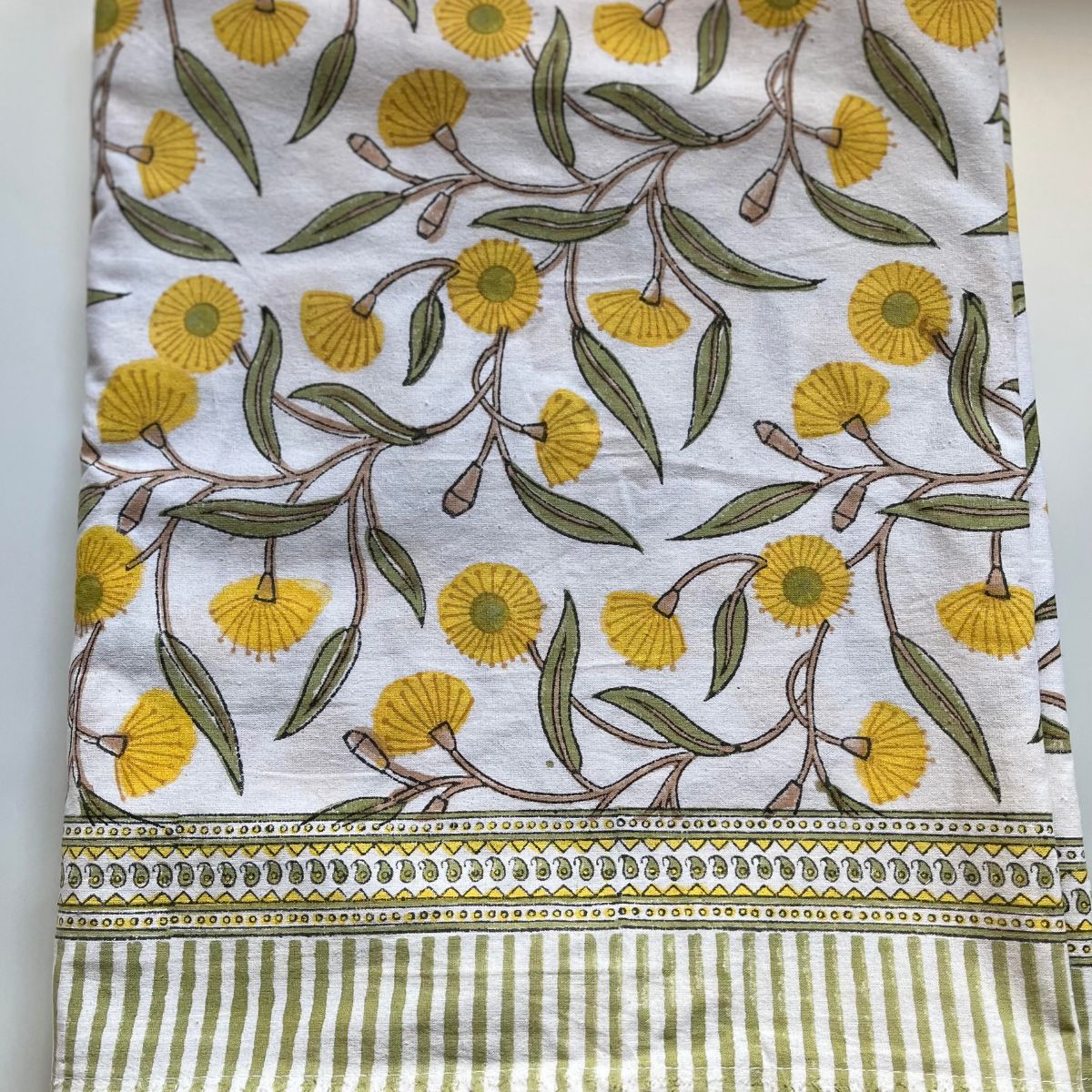 Close-up of the Yellow Flowering Gums square cotton tablecloth featuring Australian native floral motifs, geometric borders, and striped edging.