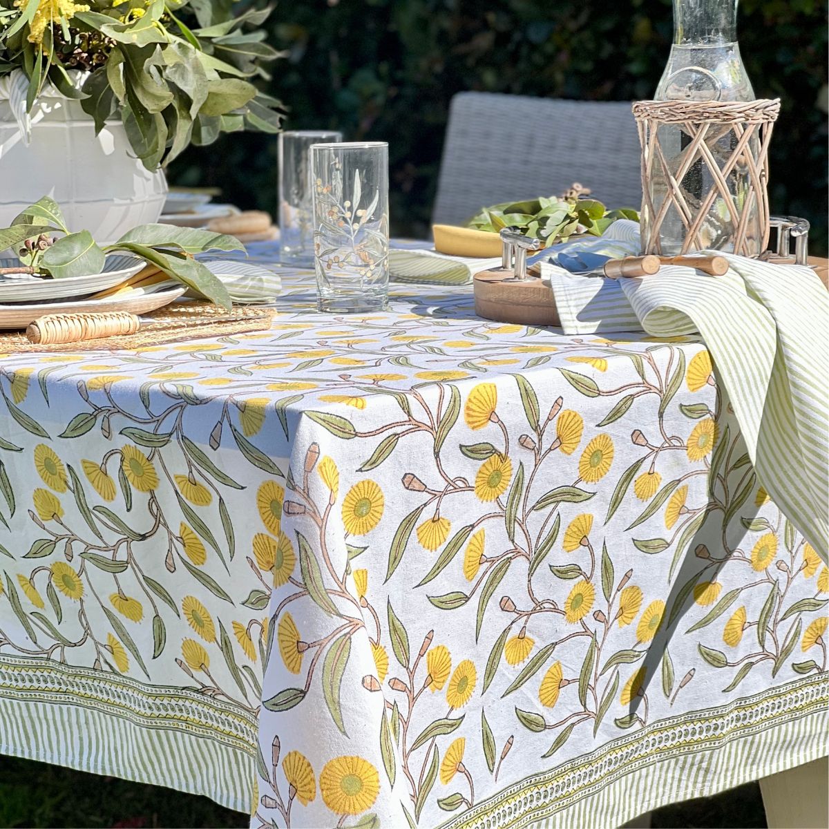 A yellow green rectangular tablecloth with a hand block printed floral pattern featuring gum trees floral pattern, displayed on a table.
